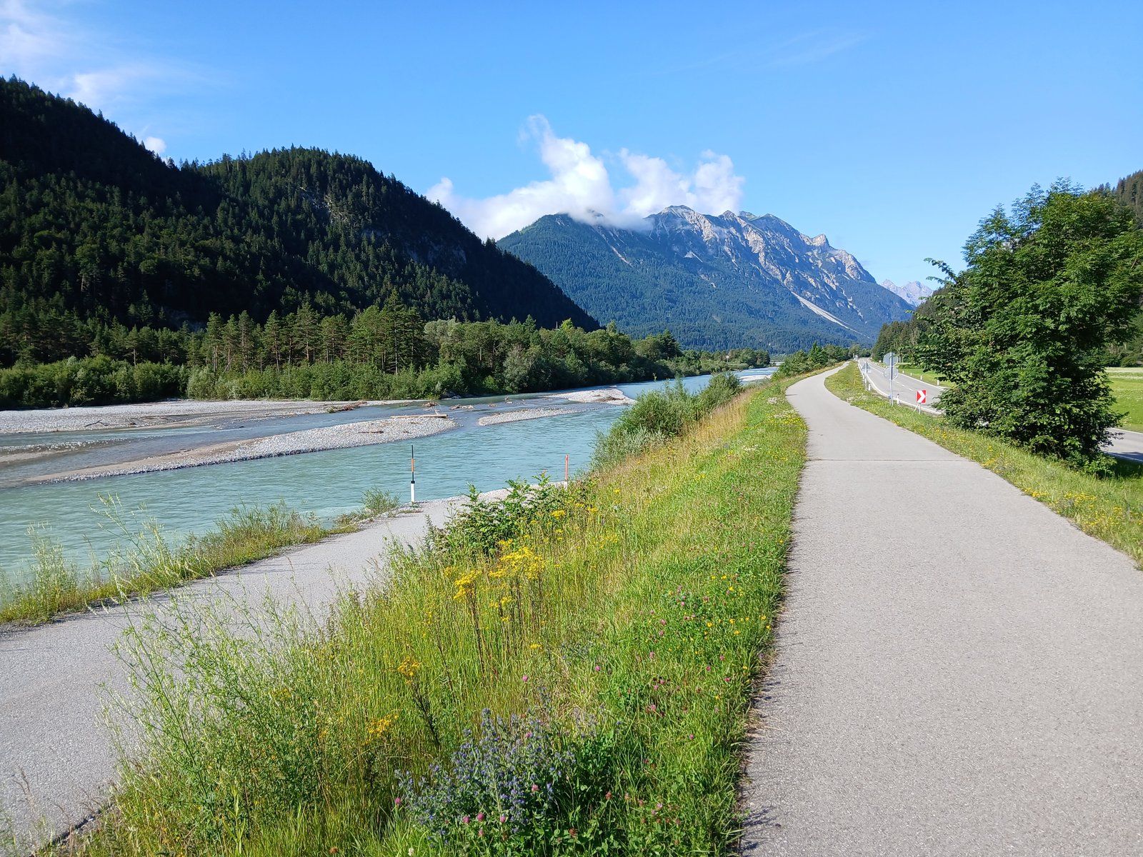 Der Lechradweg bei Höfen nahe Reutte - der asphaltierte Talweg begleitet den türkisen Wildfluss vor der Kulisse der Tiroler Alpen.