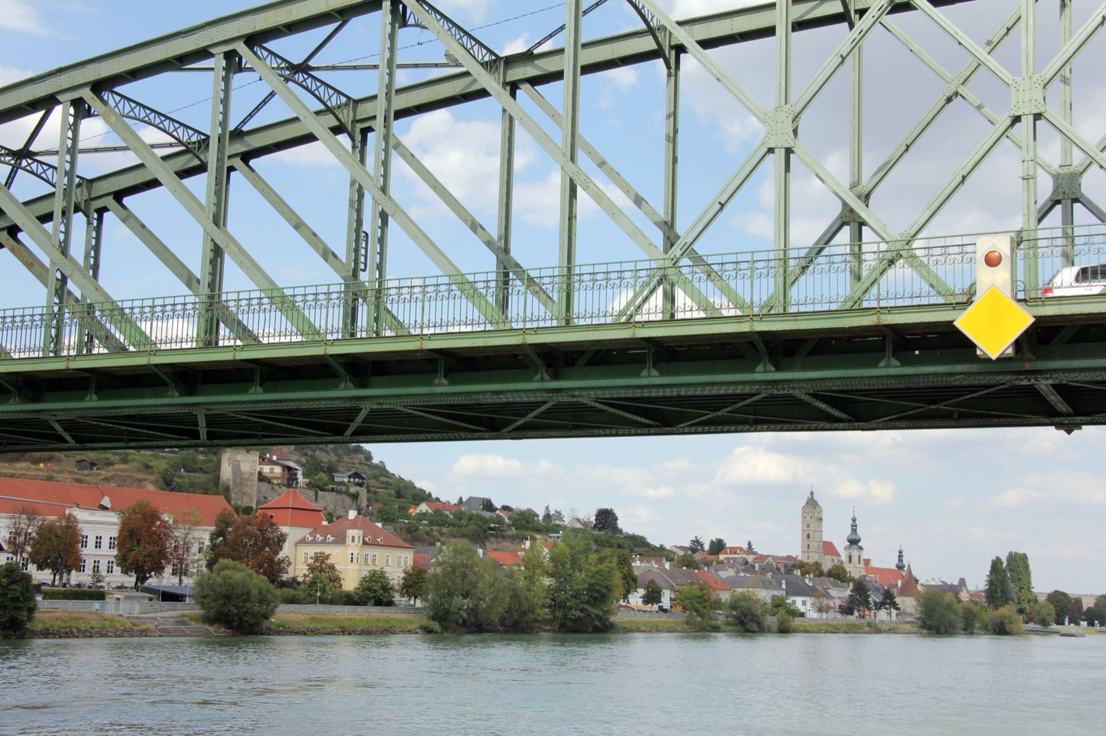 Die grüne Stahlfachwerkbrücke von Mautern über die Donau, dahinter die Altstadt von Krems-Stein, am Donauradweg in der Wachau.