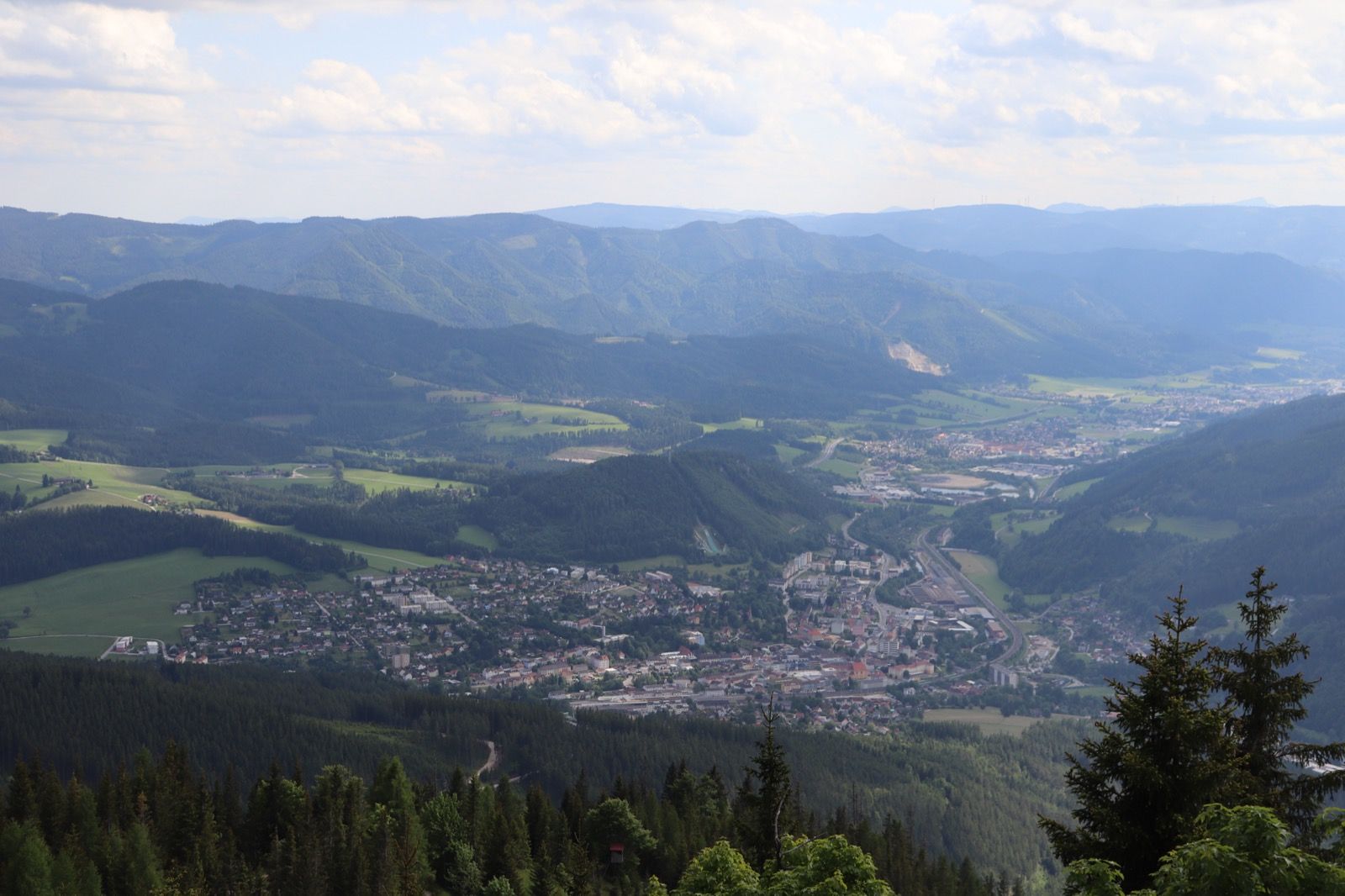 Blick von der Großen Scheibe über Mürzzuschlag und das grüne Mürztal, gerahmt von den bewaldeten Höhen der Mürzsteger und Fischbacher Alpen.